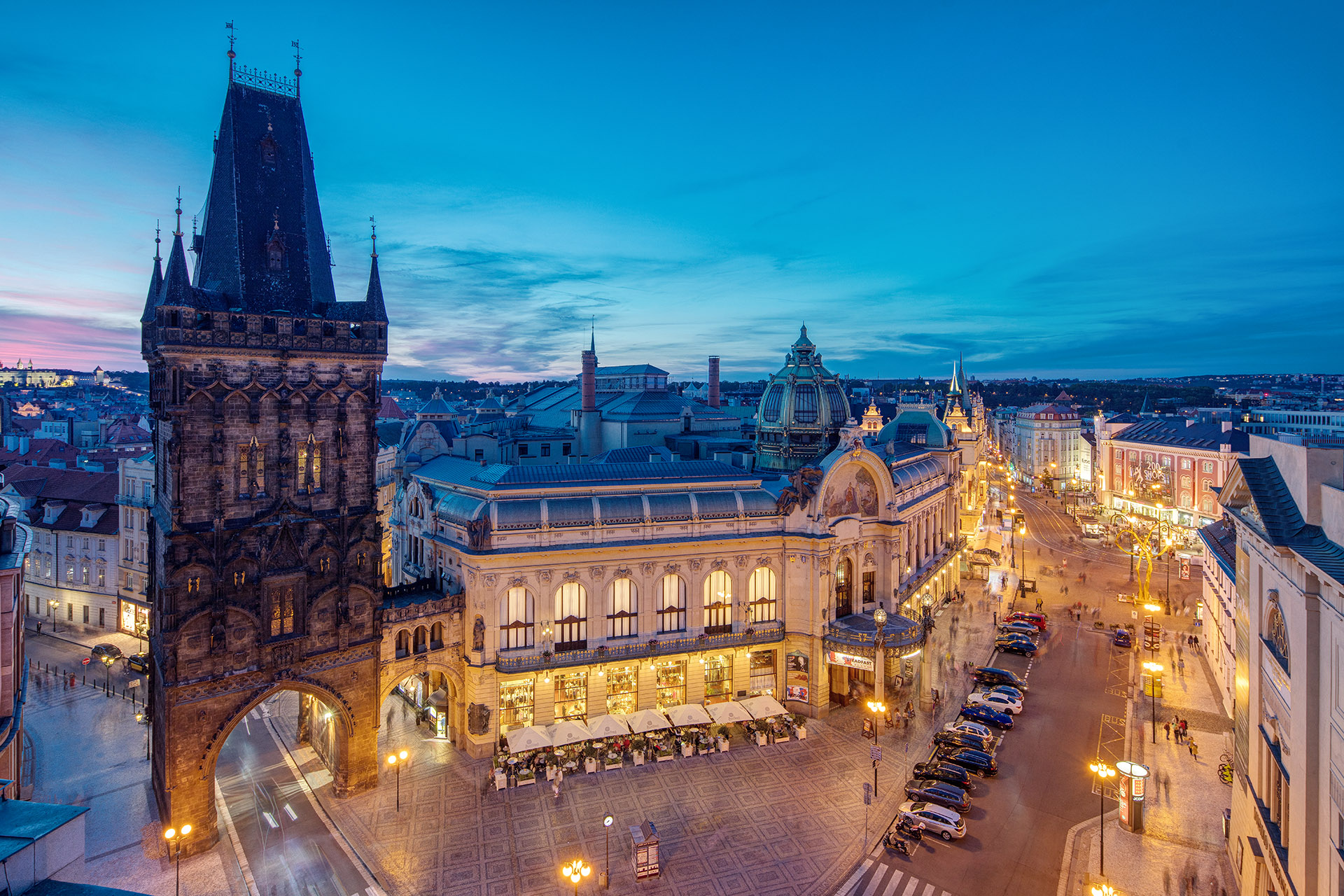 The Art Nouveau facade of the Municipal House beside the Gothic Powder Tower at dusk