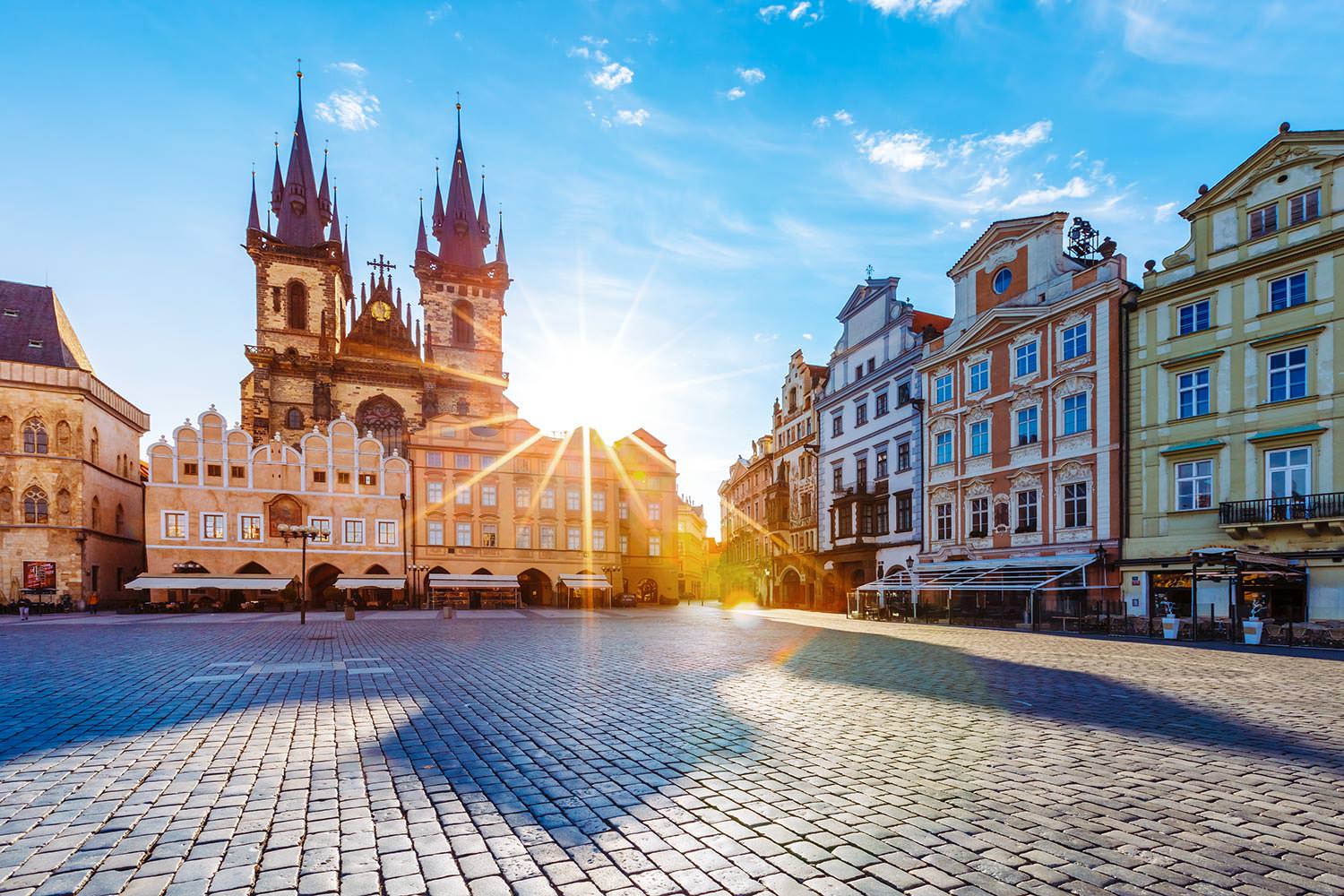 Old Town Square at sunrise, with Týn Church's Gothic spires glowing above the cobblestones